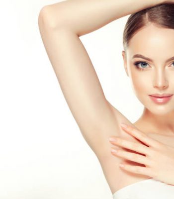 Gorgeous, young, brown haired woman with clean fresh skin and hair gathered in neat hairstyle is touching tenderly clean shaved armpit. Soft make up and light smile on the perfect face. Depilation, cosmetology and beauty technologies.